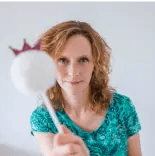 Kamila w zielonej wzorzystej bluzce, trzyma w dłoni biały długopis z pomponem i z różową koroną na czubku.